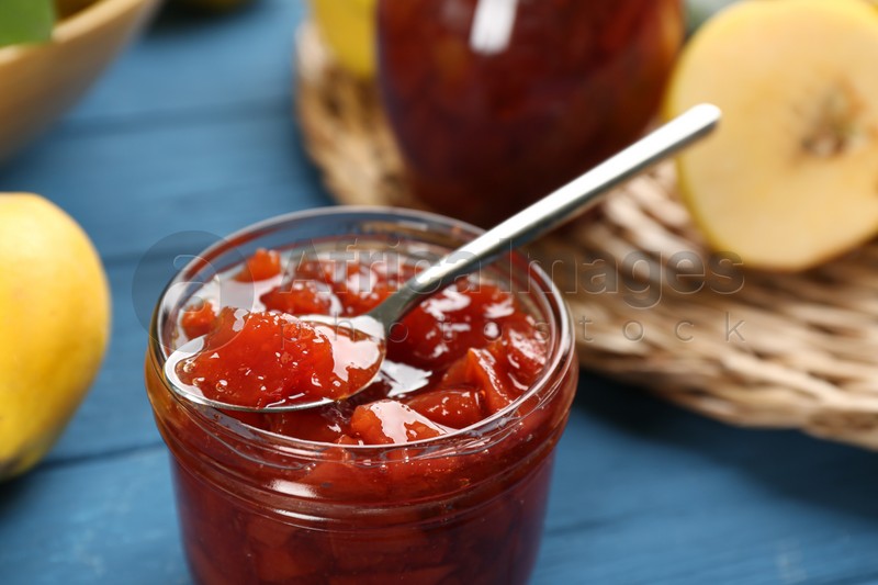 Photo of Delicious quince jam with spoon on blue table, closeup