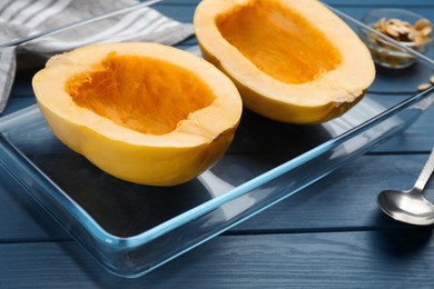Photo of Raw spaghetti squash halves in glass baking dish on blue wooden table, closeup