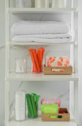 Towels, different feminine and personal care products on shelving unit in bathroom