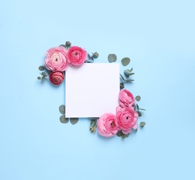 Beautiful ranunculus flowers and paper card on light blue background, flat lay. Space for text