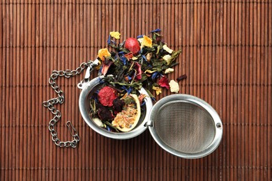 Photo of Snap infuser with dried herbal tea leaves and fruits on bamboo mat, top view