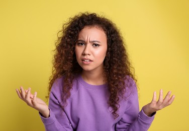 Photo of Confused African-American woman on yellow background. Thinking about difficult question