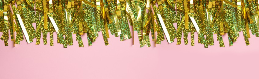Golden tinsel on pink background, top view. Banner design