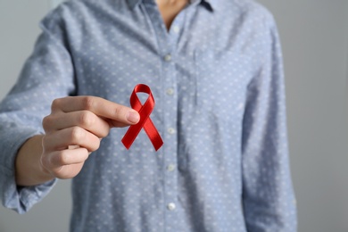 Woman holding red awareness ribbon on grey background, closeup with space for text. World AIDS disease day