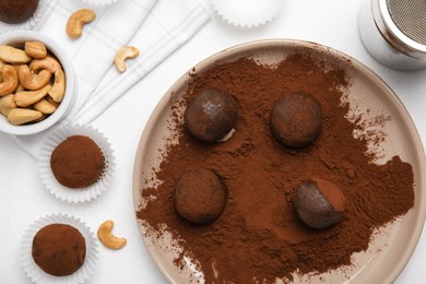 Delicious chocolate truffles with cocoa powder and nuts on white table, flat lay