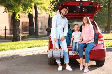 Happy family with picnic basket sitting in car's trunk on road