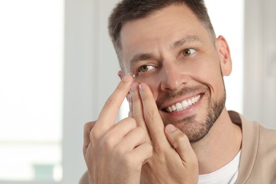 Photo of Man putting contact lens in his eye at home, space for text