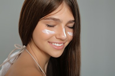 Photo of Teenage girl with sun protection cream on her face against grey background, closeup
