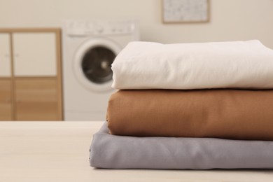 Stack of clean bed linens on white wooden table in laundry room