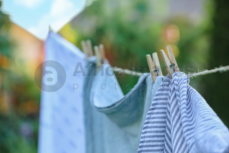 Photo of Washing line with drying shirts against blurred background, focus on clothespin