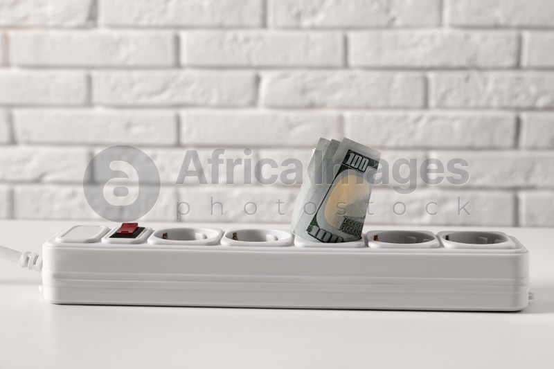 Extension board with rolled dollar banknotes on white table near brick wall