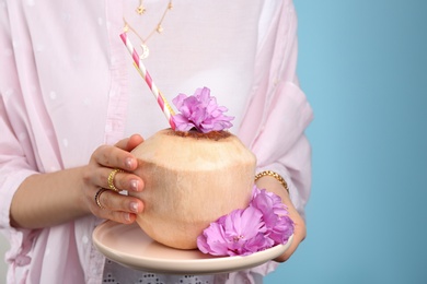 Woman holding fresh young coconut with straws on light blue background, closeup