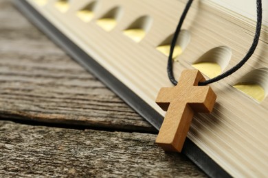 Christian cross and Bible on wooden table, closeup. Space for text