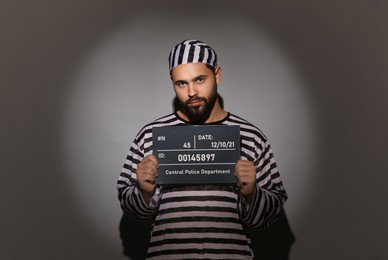 Prisoner in special uniform with mugshot letter board 
on grey background
