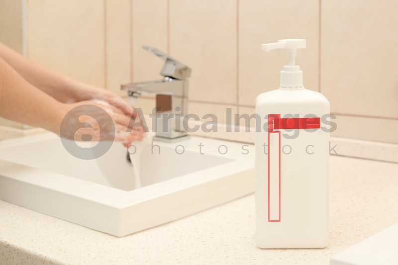 Woman washing hands in public bathroom, focus on antiseptic gel dispenser