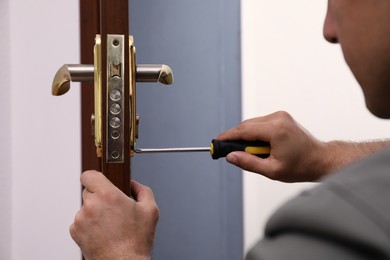 Handyman with screwdriver repairing door lock, closeup