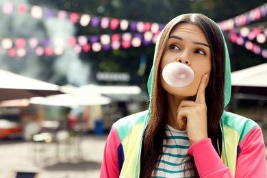 Photo of Beautiful young woman blowing chewing gum on city street outdoors