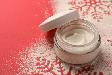 Photo of Winter skin care. Hand cream near snowflake silhouettes made with artificial snow on red background, closeup. Space for text