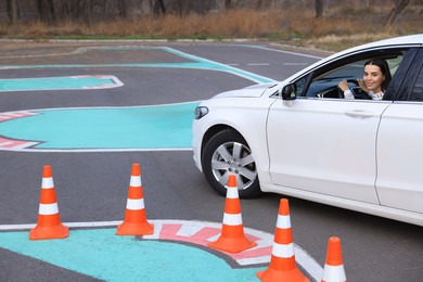 Young woman in car on test track with traffic cones. Driving school