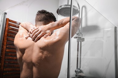 Handsome man taking shower at home, back view