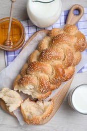 Photo of Broken homemade braided bread on white wooden table, flat lay. Traditional Shabbat challah