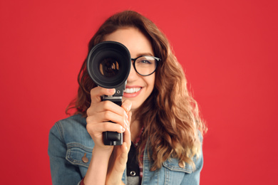 Beautiful young woman with vintage video camera against red background, focus on lens