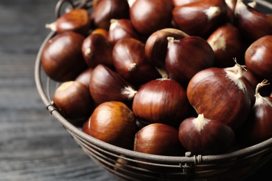 Fresh sweet edible chestnuts in basket on black table, closeup