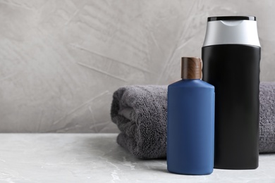 Bottles of cosmetic products and towel on light grey marble table, space for text. Men's hygiene