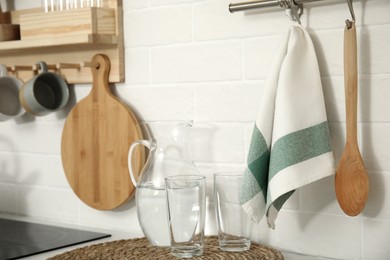 Photo of Jug with water, glasses, towel and utensils in kitchen