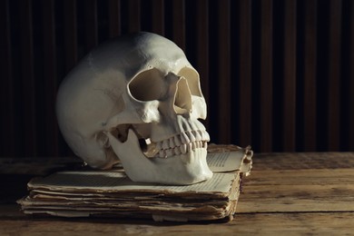 Human skull and old book on wooden table, space for text