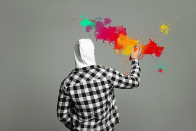 Man spraying color paints on grey background, back view