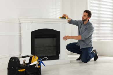 Man using construction level for installing electric fireplace near white wall in room