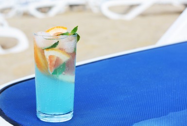 Photo of Glass of refreshing drink with grapefruit and mint on blue lounger at beach, space for text