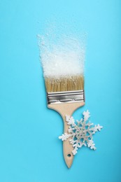 Photo of Brush painting with artificial snow on light blue background, top view. Creative concept