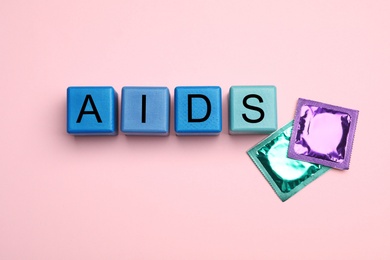 Word AIDS made with colorful cubes and condoms on pink background, flat lay. Safe sex
