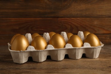 Photo of Carton with golden eggs on wooden table