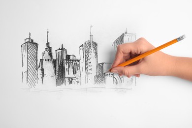 Woman drawing sketch of cityscape with graphite pencil on white paper, closeup