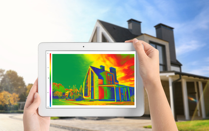 Woman detecting heat loss in house using thermal viewer on tablet, outdoors. Energy efficiency