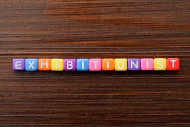 Word EXHIBITIONIST made with cubes on wooden table, flat lay