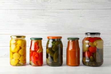 Jars with pickled vegetables on white table against wooden background