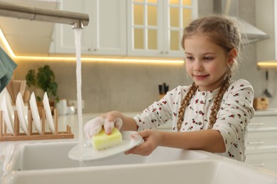 Photo of Little girl washing plate above sink in kitchen