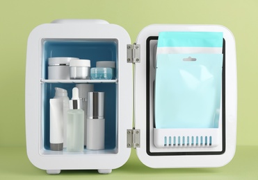 Open cosmetic refrigerator with skin care products on light green background