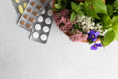 Photo of Wooden mortar with fresh herbs, flowers and pills on white table, top view. Space for text