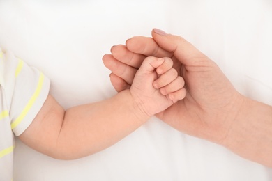 Mother holding baby's hand on bed, top view
