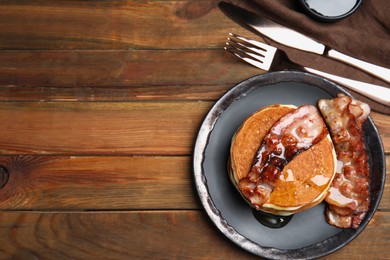 Delicious pancakes with maple syrup and fried bacon on wooden table, flat lay. Space for text