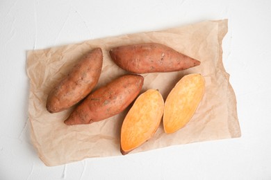 Parchment with cut and whole sweet potatoes on white table, top view