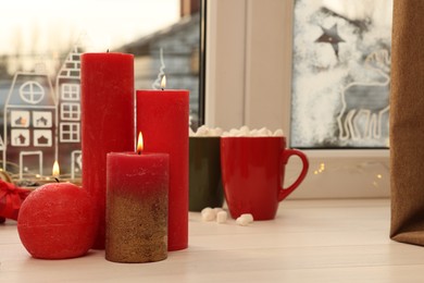 Photo of Beautiful burning candles with Christmas decor on white wooden table near window, space for text