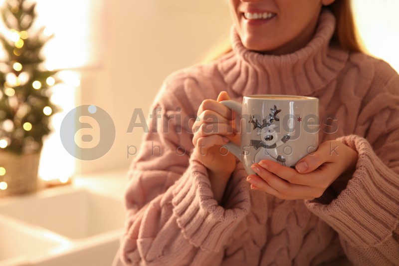 Woman holding cup with hot drink in kitchen, closeup