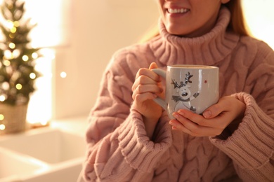 Woman holding cup with hot drink in kitchen, closeup