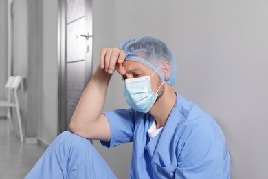 Exhausted doctor near grey wall in hospital corridor
